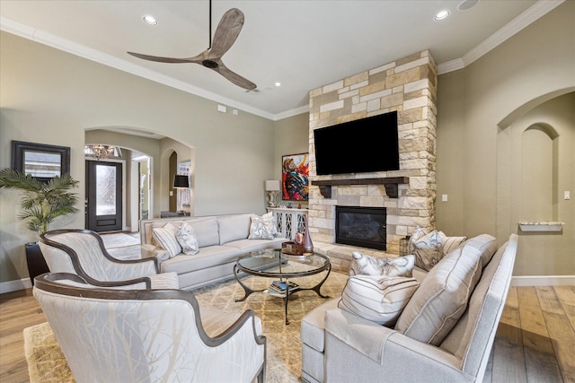 living room with ceiling fan, ornamental molding, a stone fireplace, and light hardwood / wood-style floors