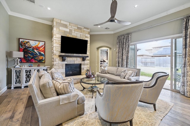 living room featuring ceiling fan, crown molding, a stone fireplace, and wood-type flooring