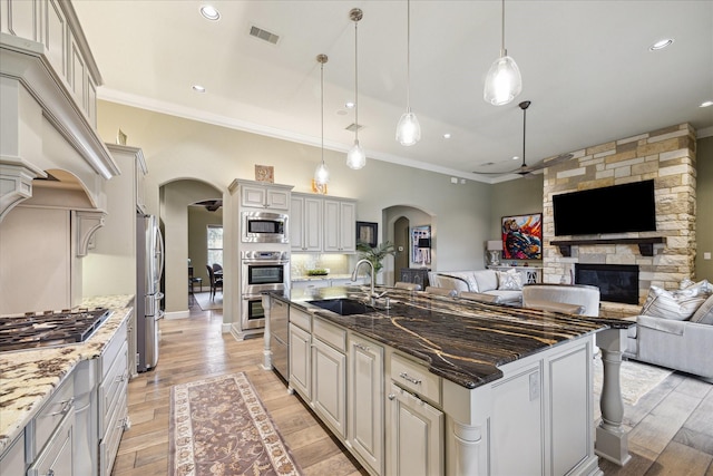 kitchen featuring appliances with stainless steel finishes, sink, dark stone counters, hanging light fixtures, and a center island with sink