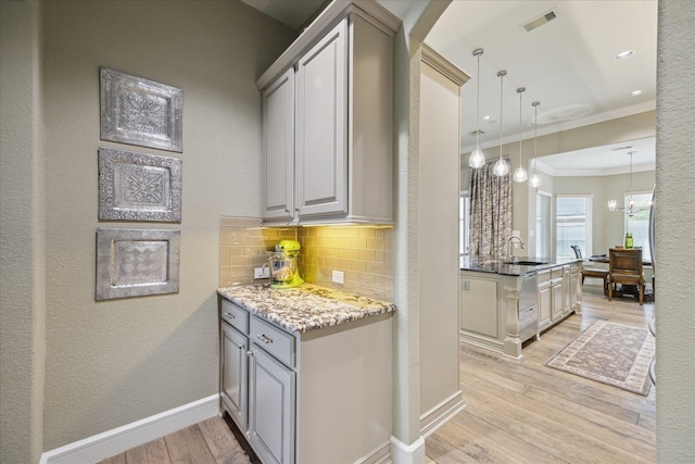 kitchen featuring sink, crown molding, backsplash, decorative light fixtures, and light wood-type flooring