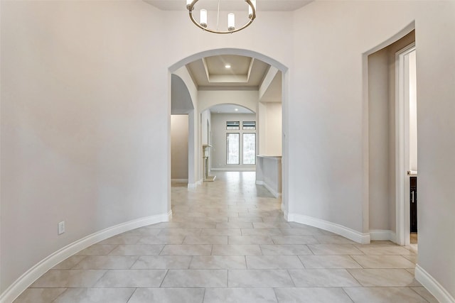 hall with a tray ceiling, light tile patterned flooring, and an inviting chandelier