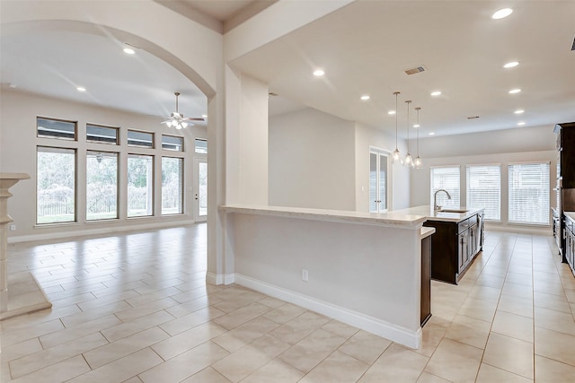 kitchen featuring ceiling fan with notable chandelier, sink, light stone countertops, an island with sink, and decorative light fixtures