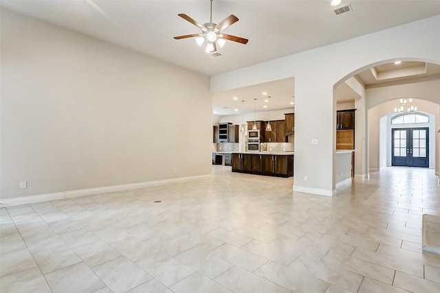 unfurnished living room with a tray ceiling, french doors, light tile patterned flooring, and ceiling fan with notable chandelier