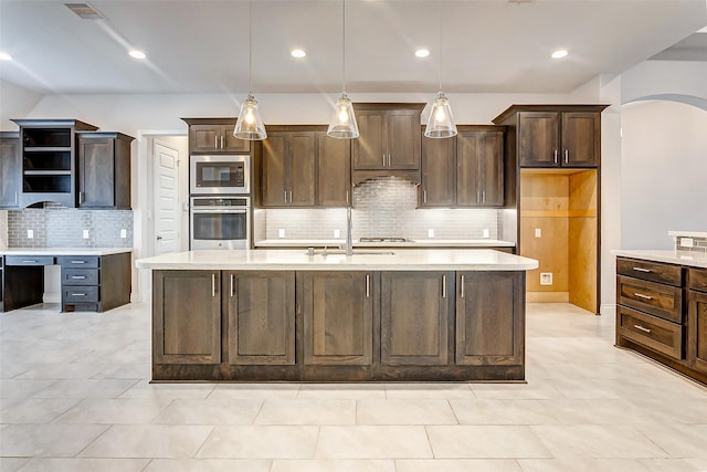 kitchen featuring dark brown cabinetry, sink, hanging light fixtures, an island with sink, and appliances with stainless steel finishes