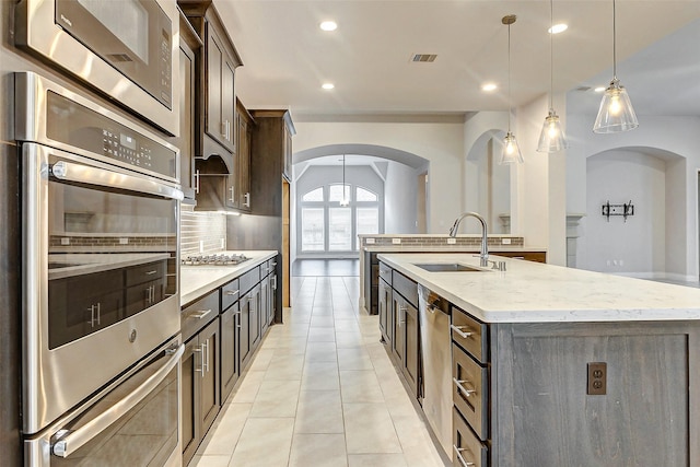 kitchen with pendant lighting, backsplash, sink, an island with sink, and appliances with stainless steel finishes