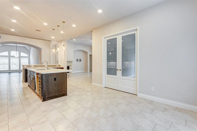 kitchen featuring pendant lighting, a center island with sink, sink, light tile patterned flooring, and dark brown cabinetry