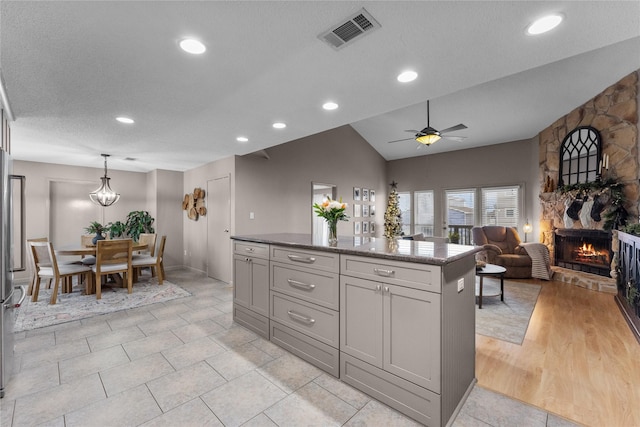 kitchen featuring hanging light fixtures, vaulted ceiling, a textured ceiling, a fireplace, and ceiling fan with notable chandelier