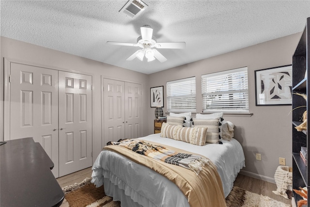 bedroom with multiple closets, ceiling fan, a textured ceiling, and light wood-type flooring