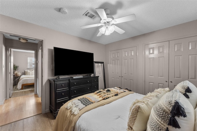 bedroom featuring hardwood / wood-style flooring, ceiling fan, a textured ceiling, and multiple closets