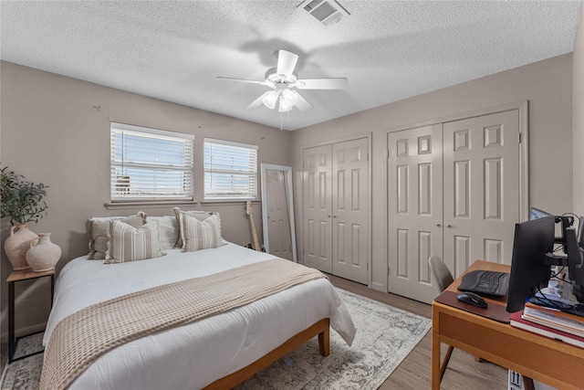 bedroom with a textured ceiling, ceiling fan, two closets, and light wood-type flooring