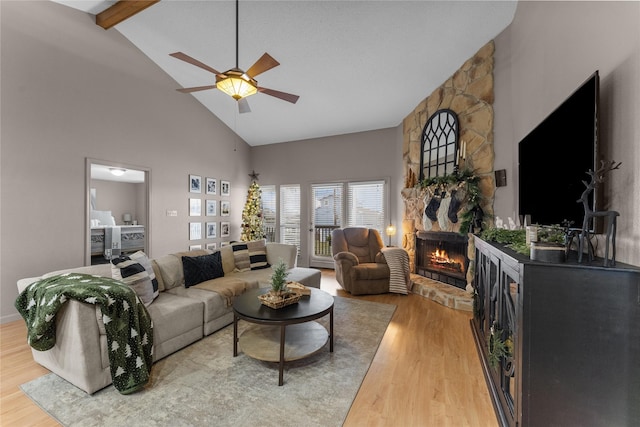 living room with ceiling fan, a stone fireplace, beamed ceiling, high vaulted ceiling, and hardwood / wood-style floors