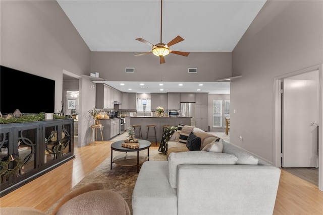 living room with ceiling fan, light hardwood / wood-style flooring, and high vaulted ceiling