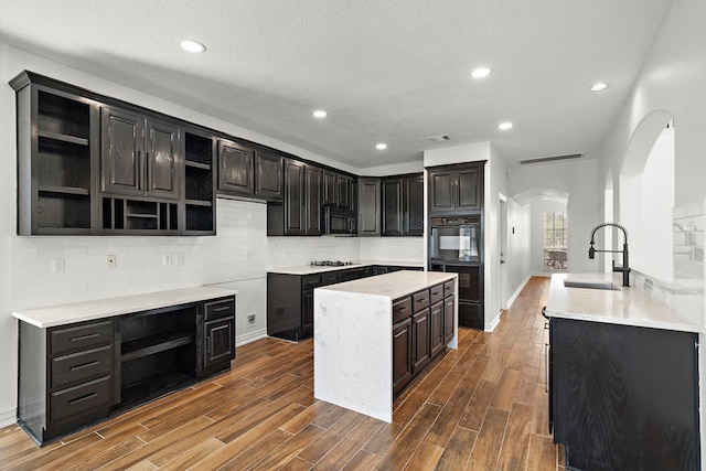 kitchen with backsplash, black appliances, sink, a textured ceiling, and an island with sink