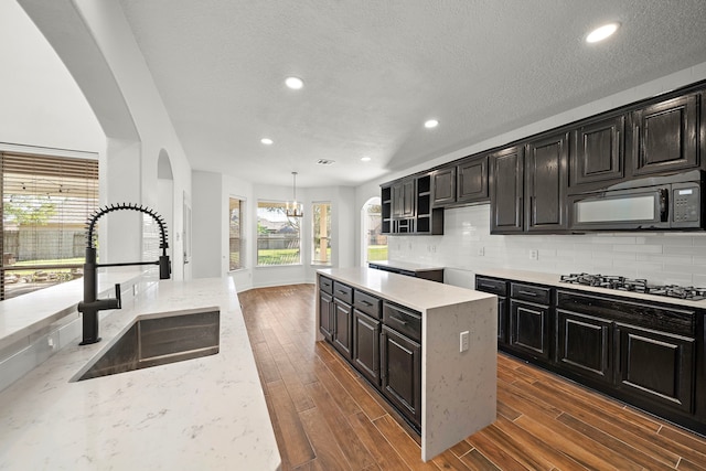 kitchen featuring backsplash, hanging light fixtures, sink, a kitchen island, and stainless steel gas cooktop