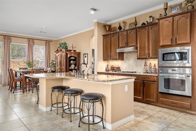 kitchen featuring stainless steel appliances, a center island with sink, light tile patterned floors, crown molding, and sink