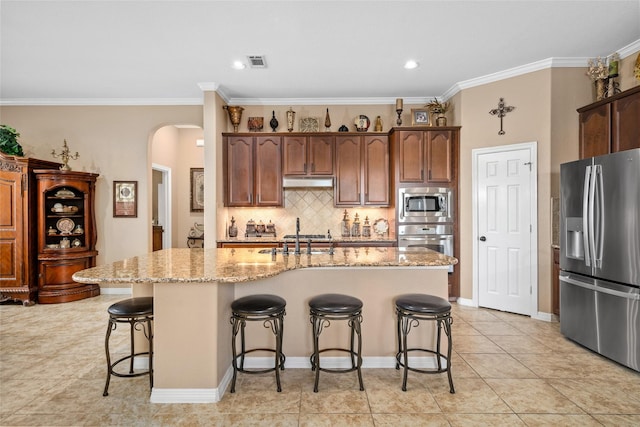 kitchen with stainless steel appliances, a kitchen island with sink, light stone countertops, and tasteful backsplash