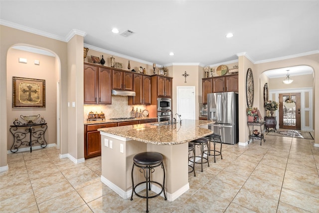 kitchen with a kitchen island with sink, a breakfast bar area, appliances with stainless steel finishes, decorative backsplash, and light tile patterned flooring