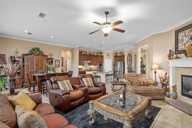 tiled living room featuring ceiling fan, ornamental molding, and a tile fireplace