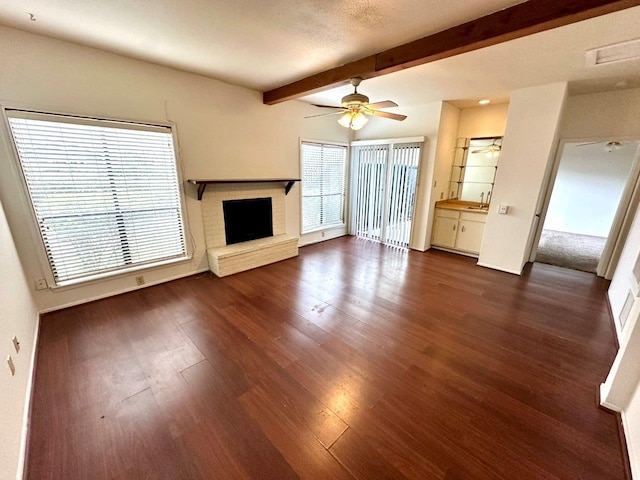 unfurnished living room with beam ceiling, ceiling fan, sink, dark wood-type flooring, and a fireplace