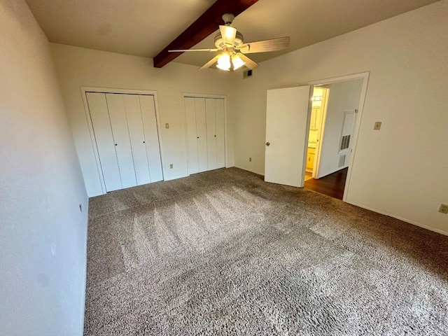 unfurnished bedroom with beamed ceiling, dark colored carpet, two closets, and ceiling fan