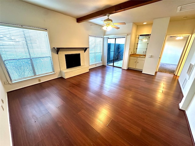 unfurnished living room with dark hardwood / wood-style flooring, a brick fireplace, beam ceiling, and ceiling fan