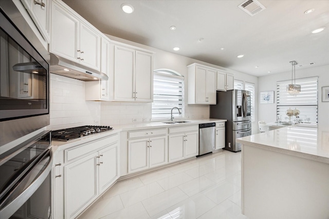 kitchen with appliances with stainless steel finishes, backsplash, sink, decorative light fixtures, and white cabinetry