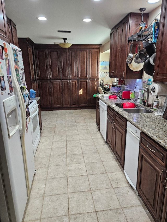 kitchen featuring light stone counters, sink, white appliances, and dark brown cabinets