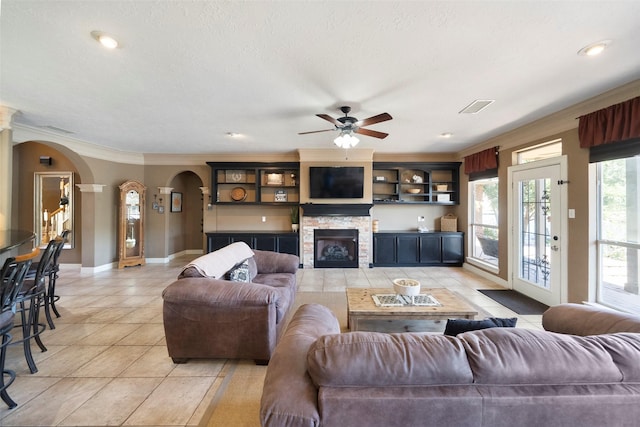 tiled living room with a stone fireplace, ceiling fan, and crown molding