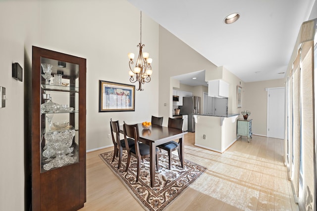 dining area featuring light hardwood / wood-style flooring, high vaulted ceiling, and an inviting chandelier