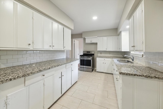 kitchen with sink, stainless steel gas range oven, stone counters, decorative backsplash, and white cabinets