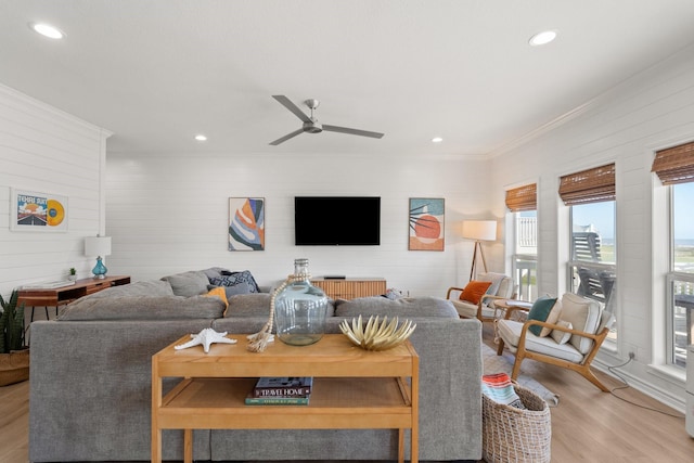 living room featuring ceiling fan, wood walls, ornamental molding, and light hardwood / wood-style flooring