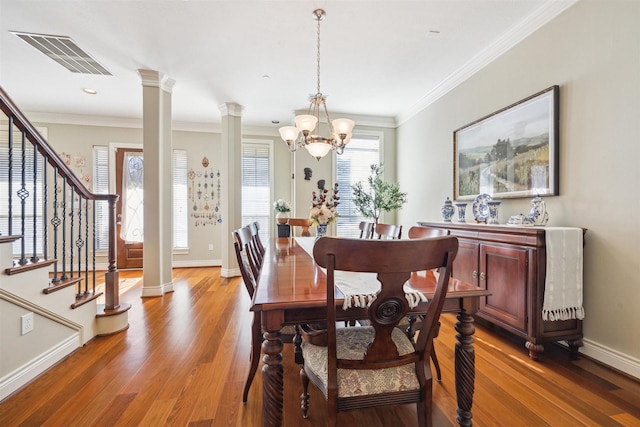 dining area with hardwood / wood-style floors, ornate columns, crown molding, and an inviting chandelier