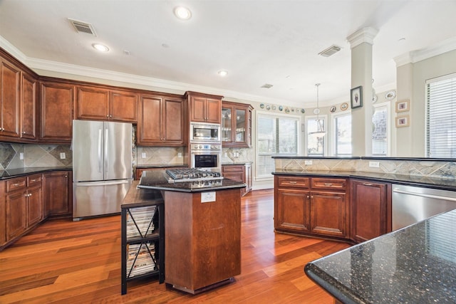 kitchen featuring dark hardwood / wood-style floors, backsplash, appliances with stainless steel finishes, a kitchen island, and ornamental molding