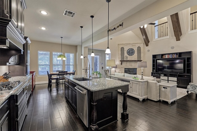 kitchen featuring light stone countertops, appliances with stainless steel finishes, pendant lighting, a fireplace, and an island with sink