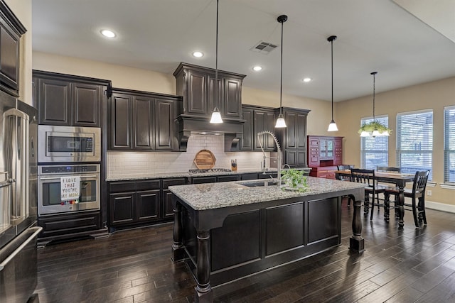 kitchen with dark wood-type flooring, hanging light fixtures, a kitchen island with sink, a breakfast bar, and appliances with stainless steel finishes