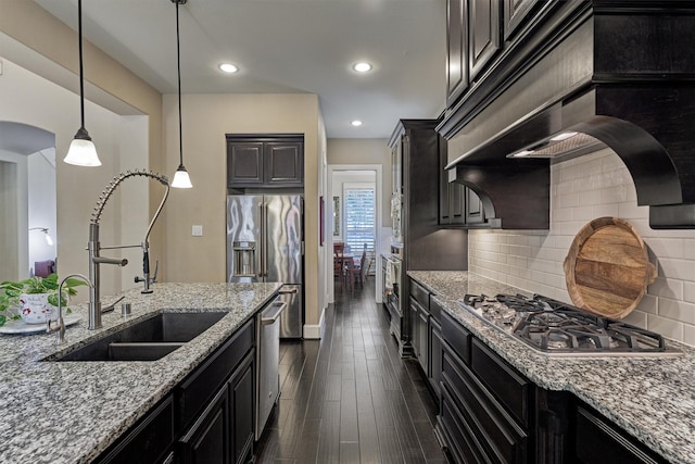 kitchen featuring light stone countertops, appliances with stainless steel finishes, dark wood-type flooring, sink, and pendant lighting