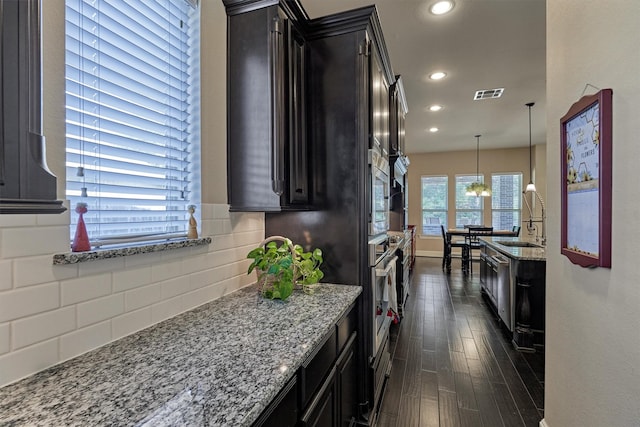 kitchen featuring dark hardwood / wood-style flooring, tasteful backsplash, light stone counters, sink, and pendant lighting