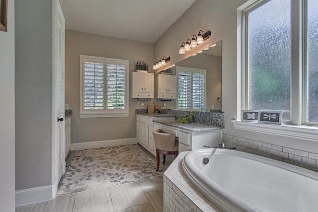 bathroom featuring vanity, a relaxing tiled tub, and a wealth of natural light