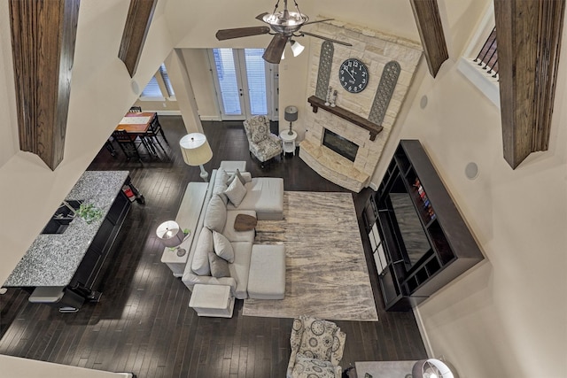 living room with a towering ceiling, hardwood / wood-style flooring, a stone fireplace, and ceiling fan