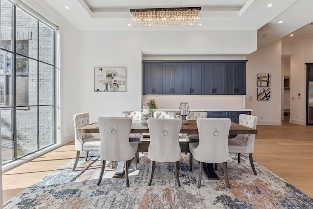 dining room featuring a tray ceiling, a notable chandelier, and light wood-type flooring