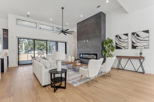 living room featuring a high end fireplace, light wood-type flooring, and ceiling fan