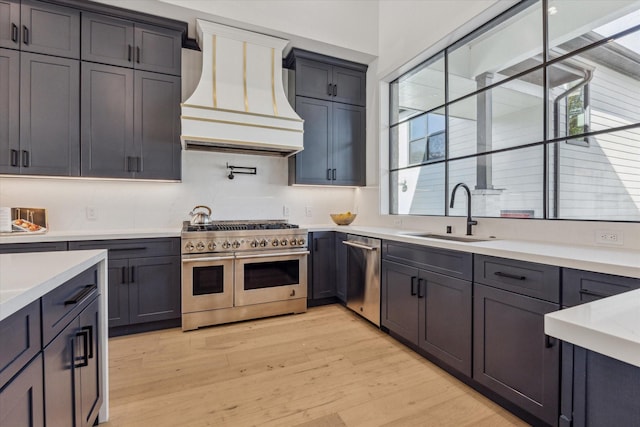 kitchen with sink, pendant lighting, light wood-type flooring, appliances with stainless steel finishes, and custom exhaust hood