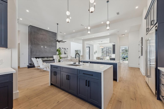 kitchen featuring ceiling fan, sink, pendant lighting, a kitchen island with sink, and a fireplace