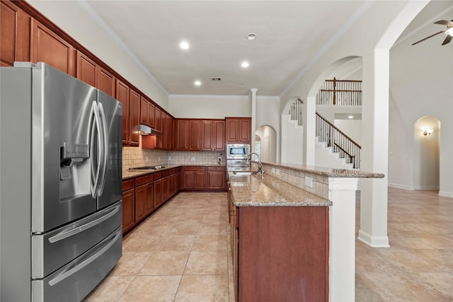 kitchen with appliances with stainless steel finishes, sink, light stone counters, ornamental molding, and an island with sink