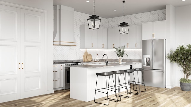 kitchen with wall chimney exhaust hood, premium appliances, a center island with sink, white cabinets, and hanging light fixtures