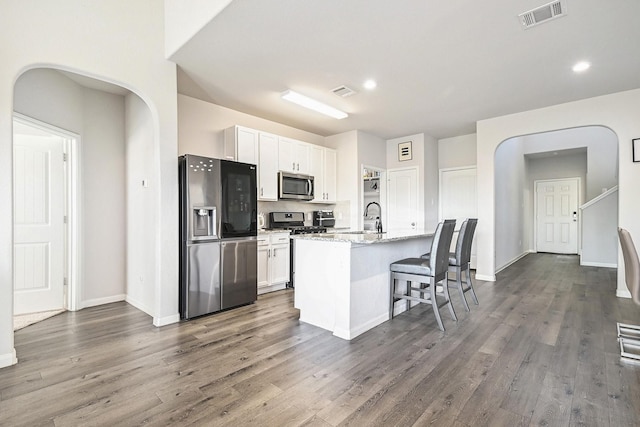 kitchen featuring white cabinets, light stone countertops, an island with sink, appliances with stainless steel finishes, and a breakfast bar area