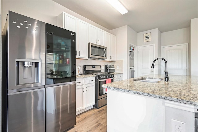 kitchen with light stone countertops, white cabinetry, sink, stainless steel appliances, and light hardwood / wood-style flooring