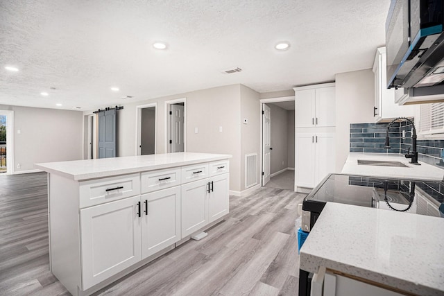 kitchen with a center island, sink, light hardwood / wood-style flooring, a textured ceiling, and white cabinetry