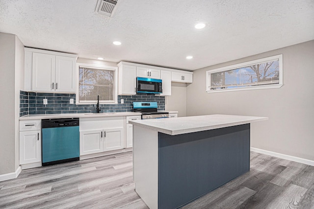 kitchen with appliances with stainless steel finishes, a textured ceiling, sink, white cabinets, and a center island