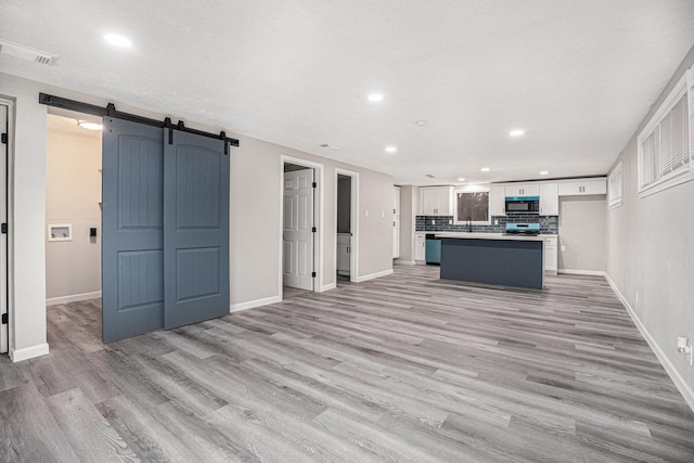 kitchen featuring backsplash, a kitchen island, a barn door, light hardwood / wood-style floors, and white cabinetry